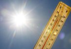 Žuti termometar pokazuje visoku temperaturu uz jako sunce i plavo nebo