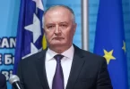 Muškarac u crnom odijelu i plavoj kravati na konferenciji pred zastavama