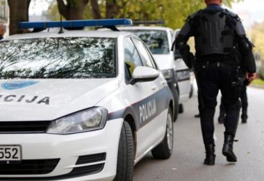 Policijski automobil Volkswagen s natpisom POLICIJA i službenik u crnoj uniformi pored vozila