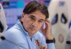 Muški trener u plavoj majici sjedeći na klupi tijekom konferencije za novinare