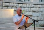 Muškarac govori na mikrofon tijekom javnog događaja ispred kamene zgrade