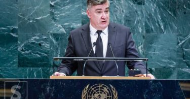 Političar na pulpitu Ujedinjenih naroda govori u mikrofonski sustav pred plavom pozadinom