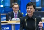 Žena u crnoj odjeći govori na konferenciji uz europske zastave i mikrofone