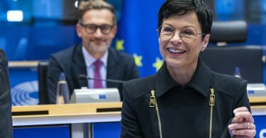 Žena u crnoj odjeći govori na konferenciji uz europske zastave i mikrofone