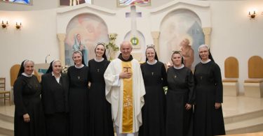 Dvije novakinje i njihova družina s crkvenim službenikom u crkvenom svetištu tijekom ceremonije zavjeta