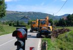 Žuta cestovna mehanizacija na lokalnoj cesti s cestovnim znakom i planinama u pozadini
