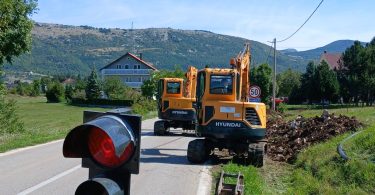 Žuta cestovna mehanizacija na lokalnoj cesti s cestovnim znakom i planinama u pozadini