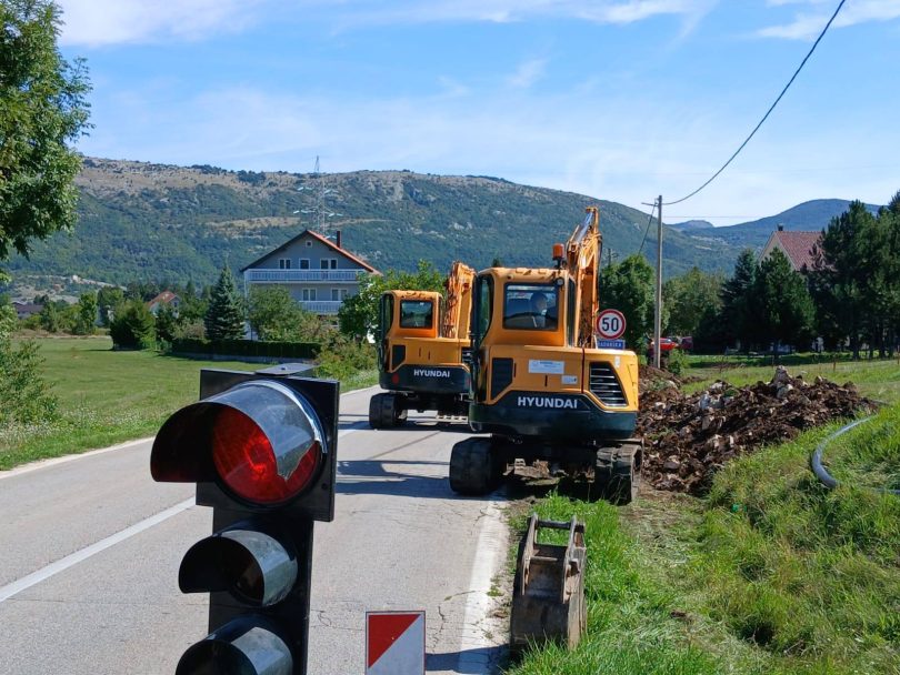 Žuta cestovna mehanizacija na lokalnoj cesti s cestovnim znakom i planinama u pozadini