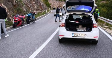 Oštećeni automobil na cesti s policajcima i drugim vozilom u pozadini
