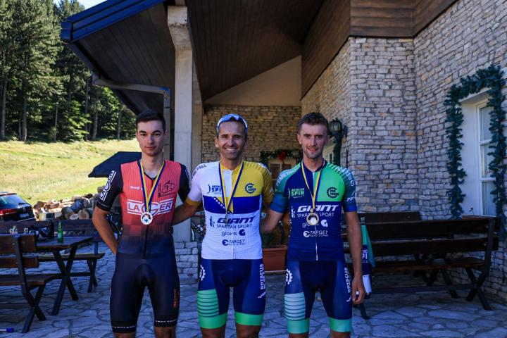Tri biciklista na podiju s medaljama; pobjednik u sredini s državnom zastavom