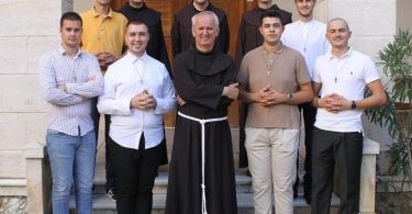 Skupina mladića i fratra u crnoj halji ispred zgrade, grupna fotografija