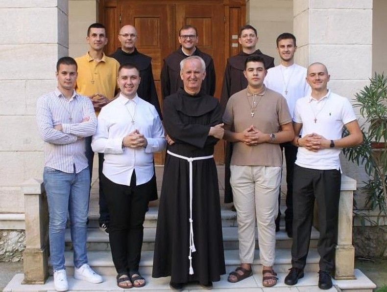 Skupina mladića i fratra u crnoj halji ispred zgrade, grupna fotografija