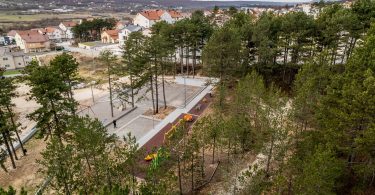 Aerial view of a modern wooden walking bridge through pine forest with town visible in background