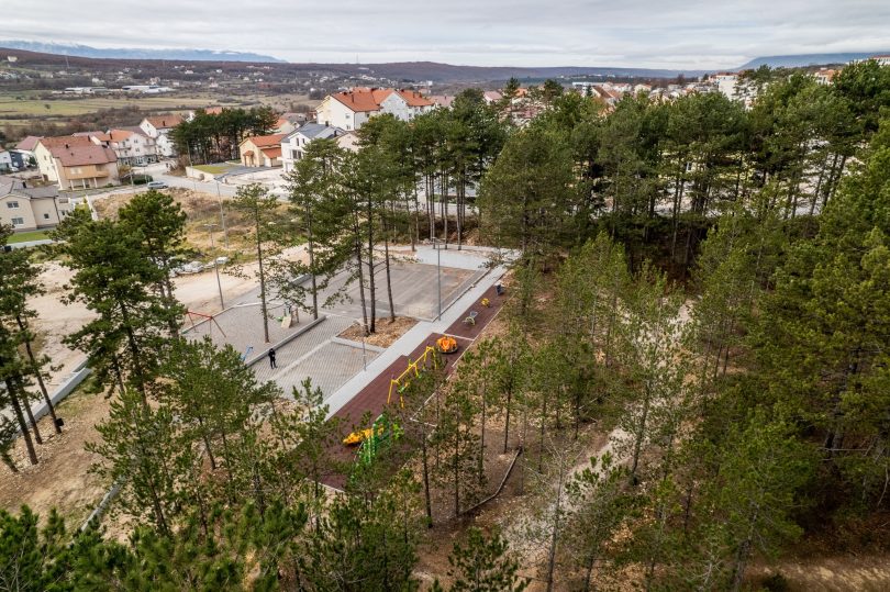 Aerial view of a modern wooden walking bridge through pine forest with town visible in background