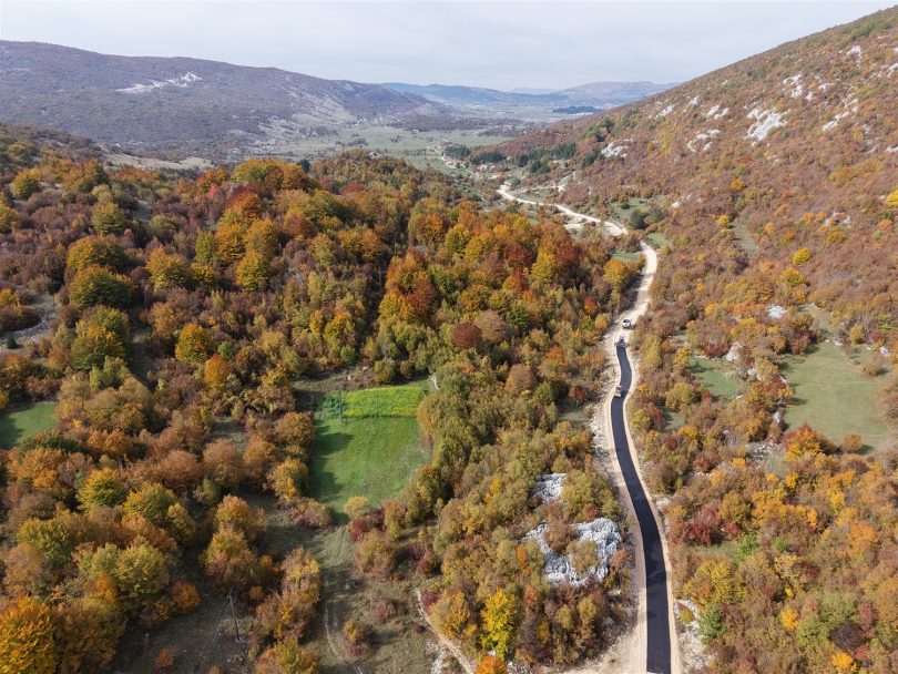 Asfaltna cesta kroz jesensku šumsku krajoliku s brežuljcima u pozadini