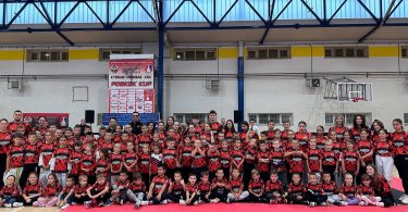 Skupine natjecatelja u crvenim dresovima poređane na teretani tijekom sportskog događaja