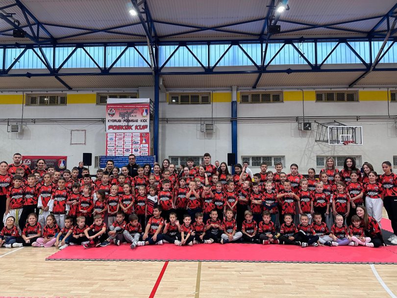 Skupine natjecatelja u crvenim dresovima poređane na teretani tijekom sportskog događaja