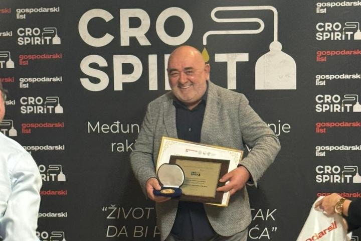 Muž sa sivom jaknom drži zlatnu diplomu na pozornici s logotipom CRO SPIRIT
