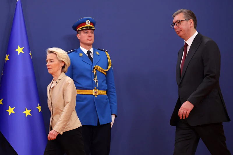 Žena u poslovnom odijelu, vojnik u plavoj uniformi i muškarac u crnom odijelu ispred EU zastave