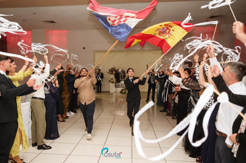 Skupina gostiju na svatbi s hrvatskim i španjolskim zastavama, tradicijski domaćinski doček