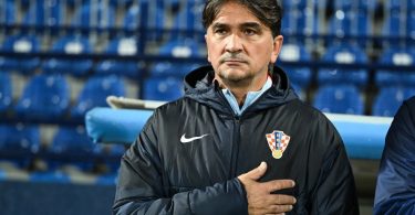 Trener u crnoj jakni sa znakom hrvatske nogometne reprezentacije, ruke na prsima, na klupi tijekom utakmice