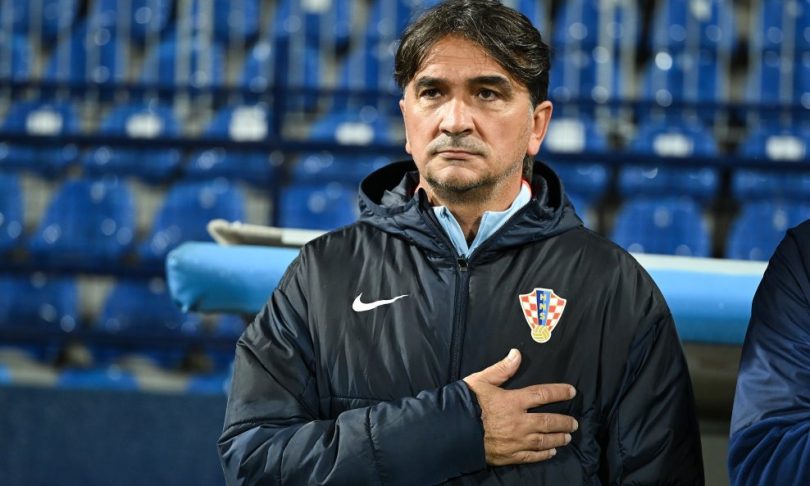 Trener u crnoj jakni sa znakom hrvatske nogometne reprezentacije, ruke na prsima, na klupi tijekom utakmice
