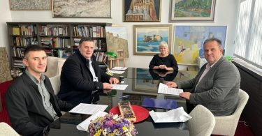 Četiri osobe za stolom tijekom potpisivanja ugovora, s cvijećem i dokumentima