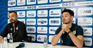 Dvije osobe na konferenciji za medije, muškarac s mikrofonom govori iznad stola s logotipima sponzora