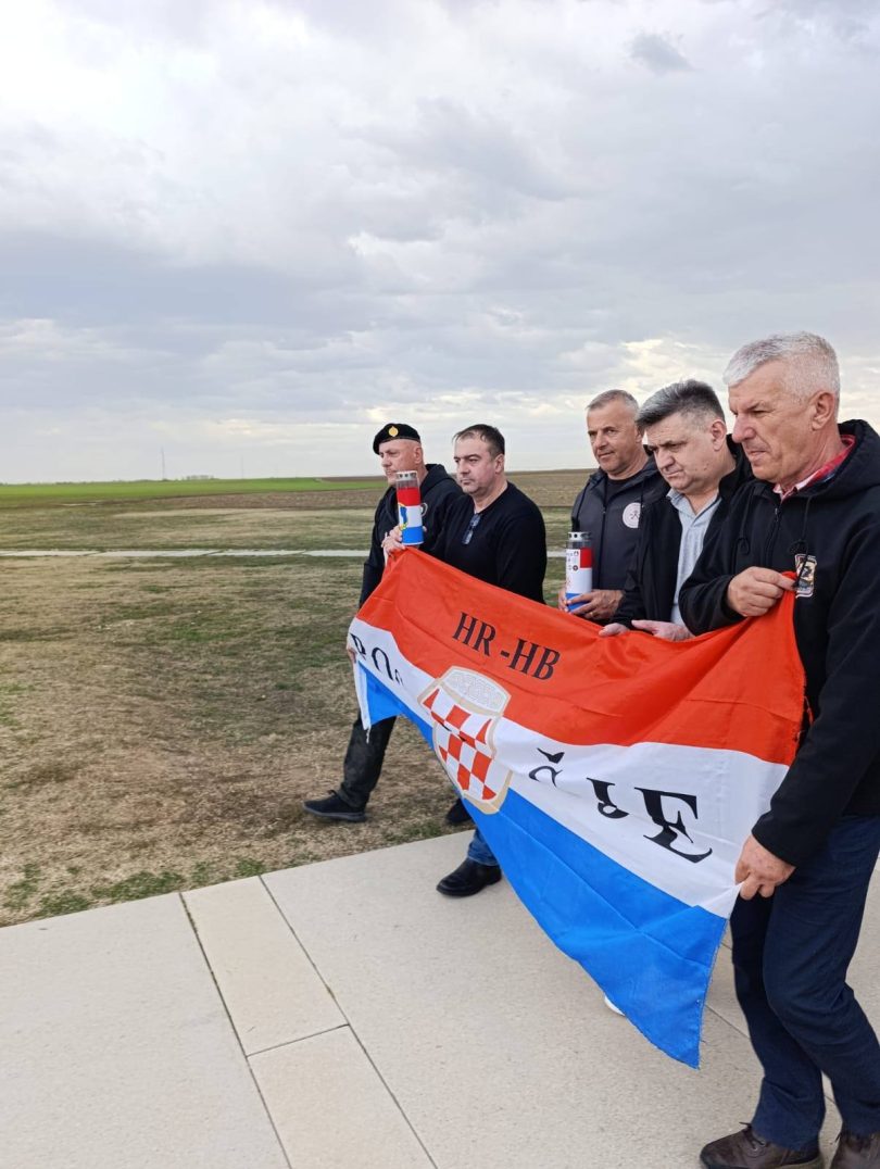 Zvaničnici i građani drže hrvatsku zastavu na otvorenom polju tokom komemorativne ceremonije