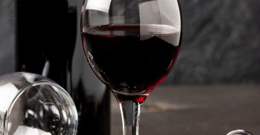Čaša crvenog vina pored otvorene boce i čepa na sivoj površini