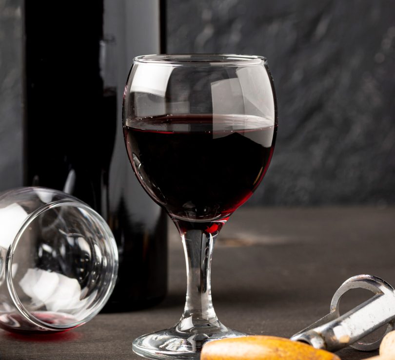 Čaša crvenog vina pored otvorene boce i čepa na sivoj površini