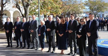 Službeni i građani u crnoj odjeći stoje u nizu tijekom komemorativne ceremonije na javnoj površini.
