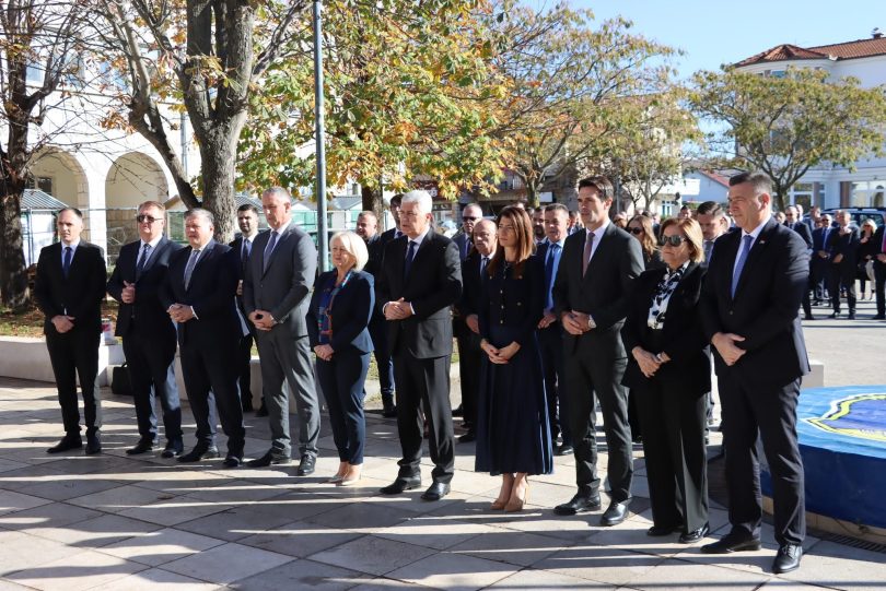 Službeni i građani u crnoj odjeći stoje u nizu tijekom komemorativne ceremonije na javnoj površini.
