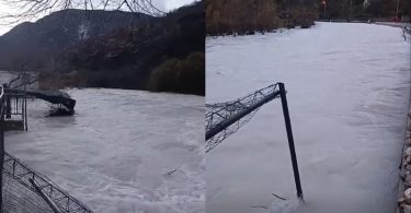 Zamrznutu rijeku prekriva led i snijeg, mostić u pozadini, brdska područja prekrivena snijegom