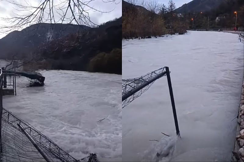 Zamrznutu rijeku prekriva led i snijeg, mostić u pozadini, brdska područja prekrivena snijegom