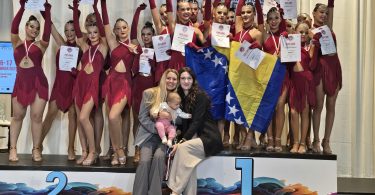 Grupa mladih plesačica u crvenim kostimima s medaljama i certifikatima pozira za fotografiju.