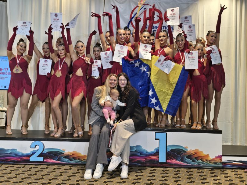 Grupa mladih plesačica u crvenim kostimima s medaljama i certifikatima pozira za fotografiju.