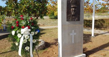Sivi kameni spomenik s portretom i križem, pred njim bijeli vijenci cvijeća