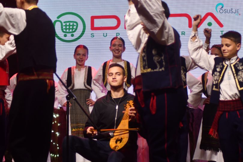 Glazbenik sa gitarom na sceni okružen tradicijskim nošnjama tijekom božičnog programa
