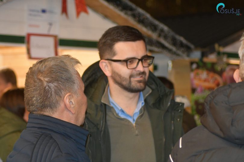 Muškarci u zimskoj odjeći razgovaraju na događaju u zatvorenom prostoru.