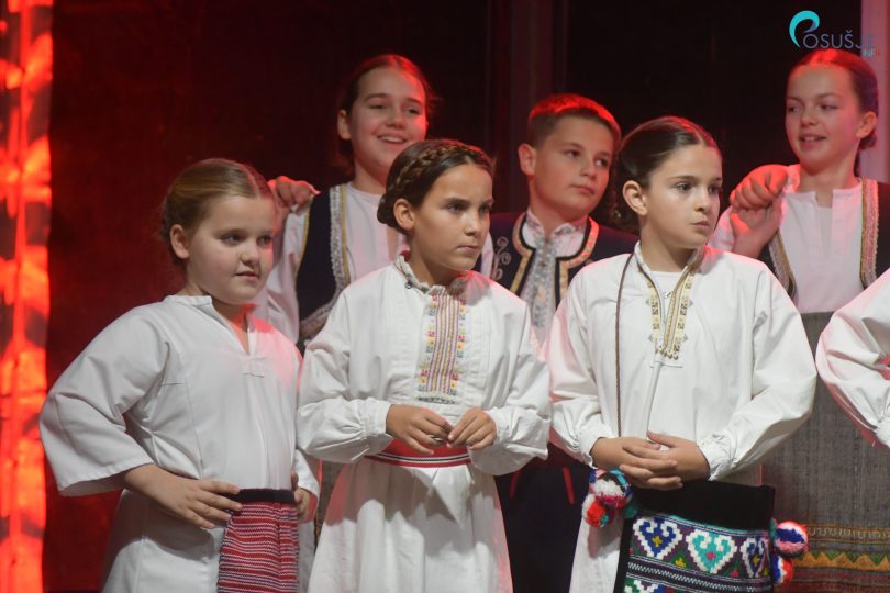 Skupina djece u bijelim tradicionalnim košuljama i crvenim detaljima tijekom božićne manifestacije