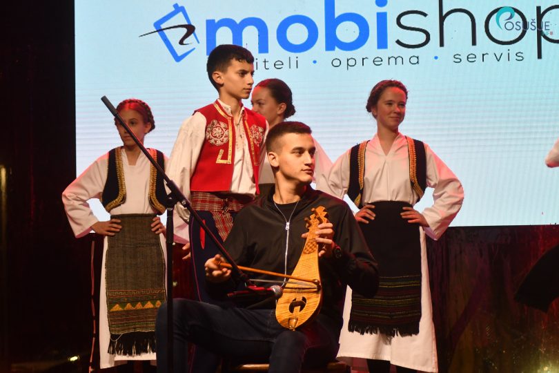 Mladić svira violinu na pozornici, u pozadini ostali sudionici manifestacije