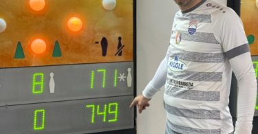 Muškarac pored elektronskog rezultatskog panela sa brojem 749 na sportskoj areni