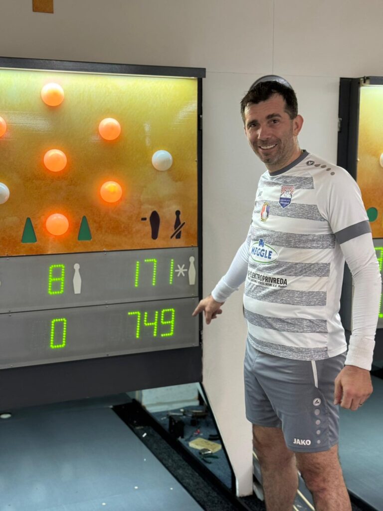 Muškarac pored elektronskog rezultatskog panela sa brojem 749 na sportskoj areni