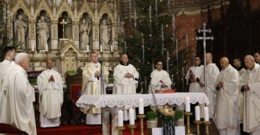 Nadbiskup Vrhbosanski Vinko Vukšić u liturgijskom odjeću tijekom mise, okružen svećenicima pred oltarom украšenim cvijećem