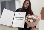 Žena u crnoj odjeći s diplomom i cvijećem, dobitnica univerzitetske nagrade