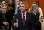 Andrej Babiš u tamnom odijelu i crveni kravati drži čašu tijekom ceremonije