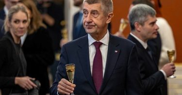 Andrej Babiš u tamnom odijelu i crveni kravati drži čašu tijekom ceremonije