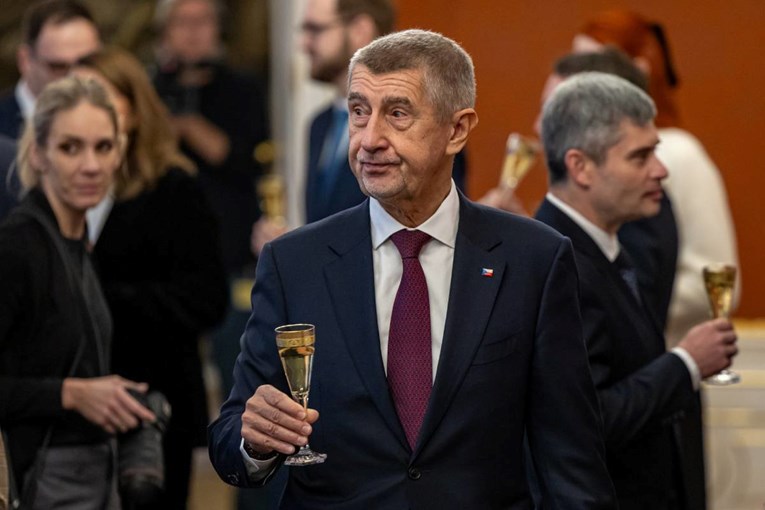 Andrej Babiš u tamnom odijelu i crveni kravati drži čašu tijekom ceremonije