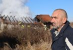 Muškarac stoji ispred izgorjele kuće s oteglinama u pozadini